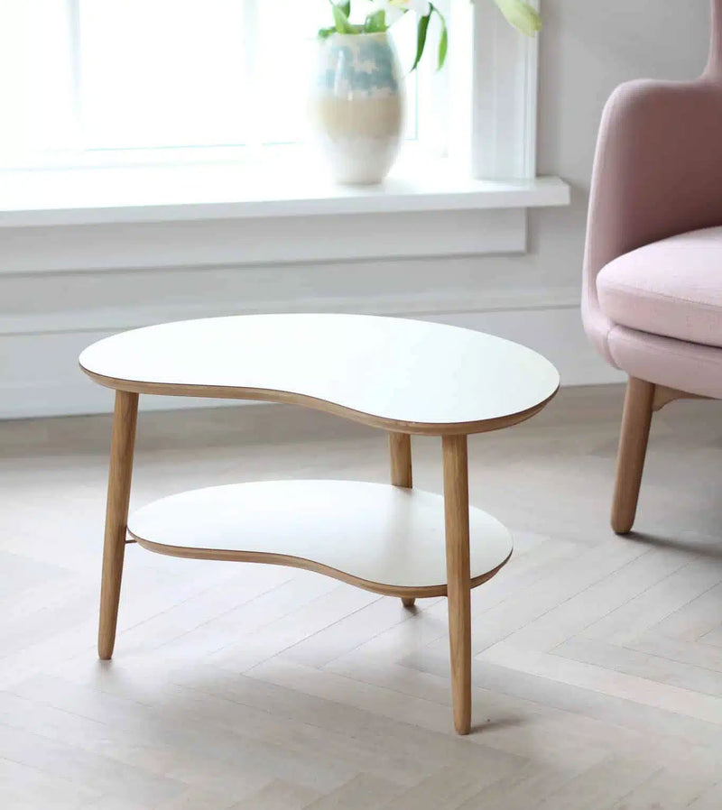 Elegant hvidt Bønnebord sofabord i laminat, lille model med lav hylde, designet af Karsten Lauritsen. Dette designer sofabord har en karakteristisk organisk form og elegante lyse egetræsben. Perfekt som et let og stilrent sofabord. Se vores udvalg af hvide sofaborde her.